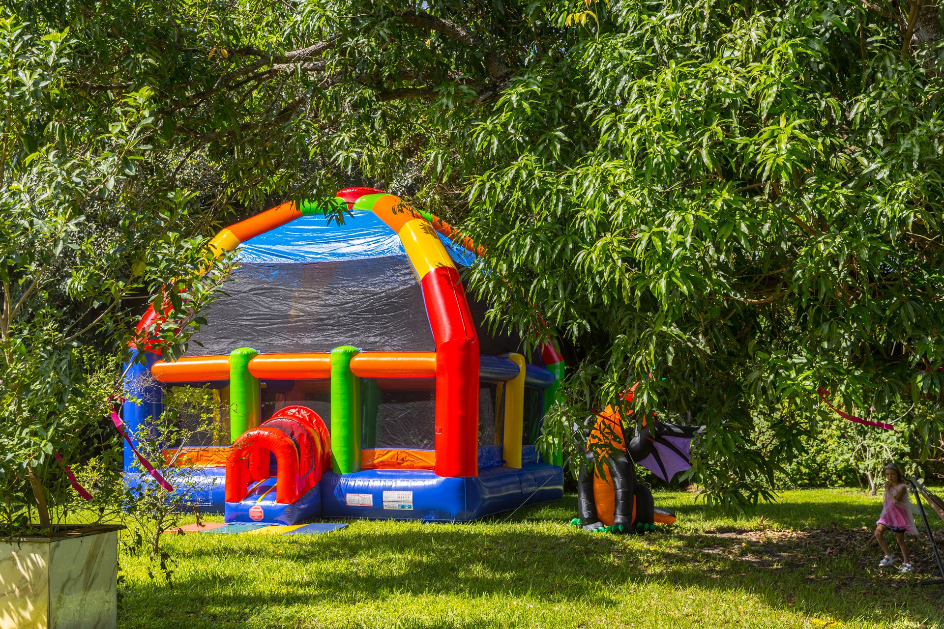 The colourful bounce house set up in the shade of tall trees, still empty