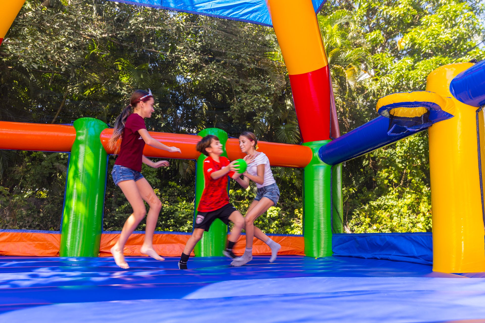 Three children leap after a ball inside a big inflatable bounce house