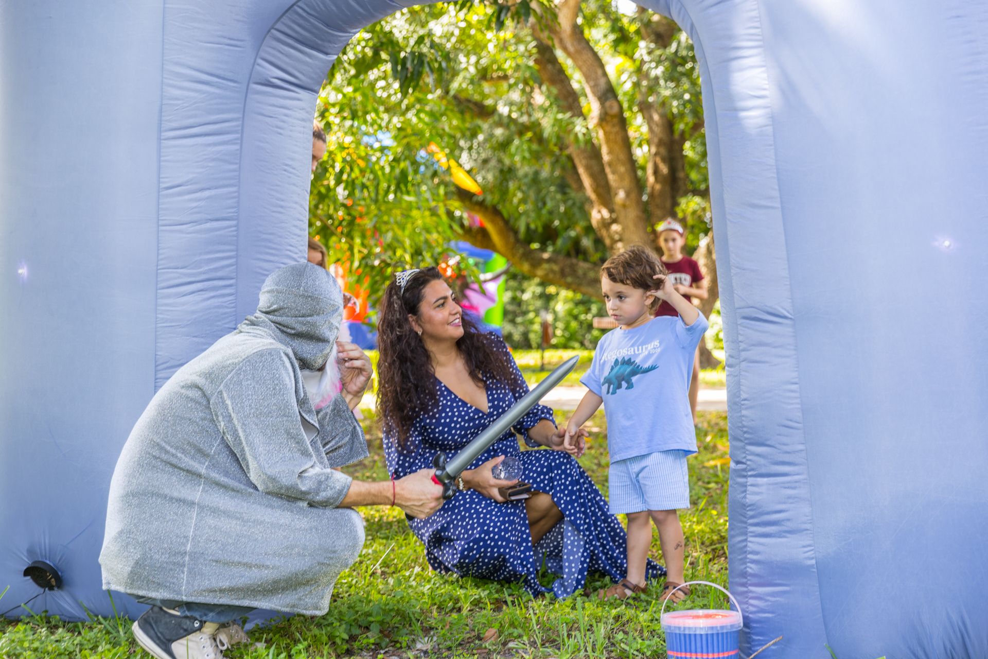 The wizard in a silver hood kneels to talk with a mother and her son by an inflatable arch