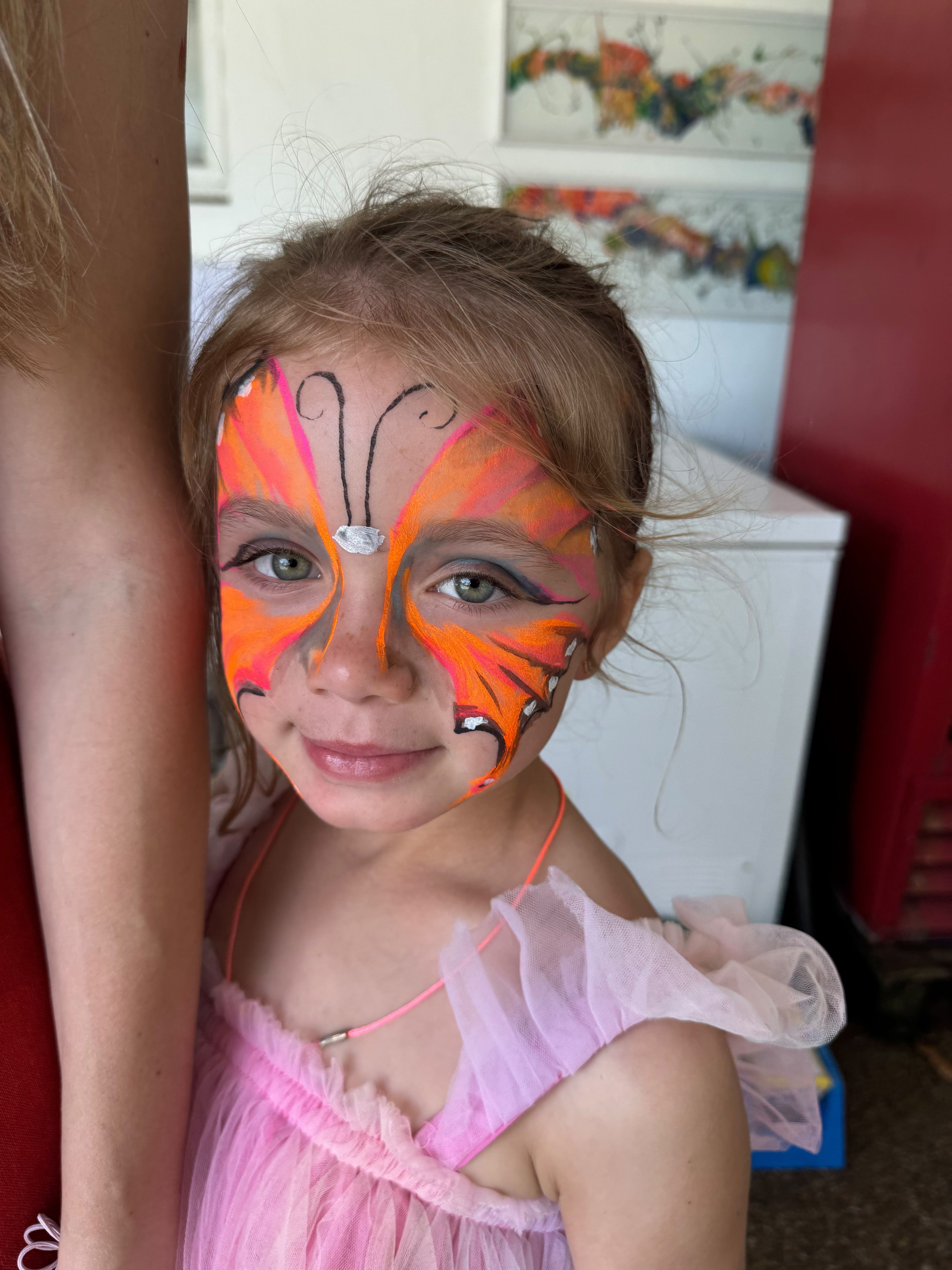 Close-up of a smiling girl with an orange butterfly painted across her face
